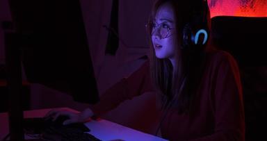 为球员玩家年轻的亚洲女人玩在线视频游戏拍摄帧/秒比赛排名网络互联网晚上红色的霓虹灯光房间游戏耳机键盘冠军事件